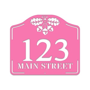 May include: Pink metal house number sign with white lettering. The sign features the number 123 and the street name "MAIN STREET" with an acorn and oak leaf design at the top.