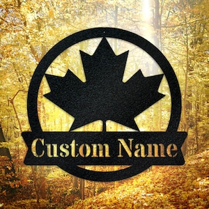 May include: Black metal sign with a maple leaf design and a banner that says "Custom Name".
