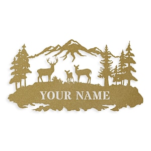 May include: A gold metal silhouette of a mountain range with two deer and a fawn standing in front of a forest. The text "YOUR NAME" is below the deer.