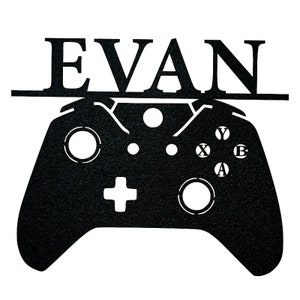 Pode incluir: Silhueta de metal preto de um controlador de videogame com o nome "EVAN" acima.