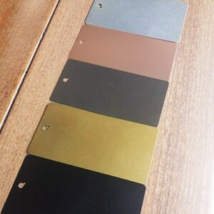 May include: Five metal samples in different colors, arranged in a row from top to bottom: light blue, brown, dark gray, gold, and black.