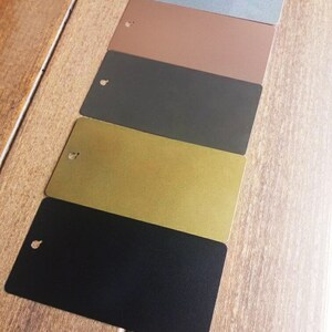 Pode incluir: Cinco pequenas amostras retangulares de tinta de diferentes cores. As cores s&atilde;o azul claro, marrom, cinza escuro, dourado e preto.