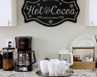 May include: A black, decorative wall sign with a scalloped edge featuring the text "OLD FASHIONED Hot Cocoa SERVED HERE" in a light-colored script and serif font, accented with small snowflake illustrations and a central cocoa mug icon.