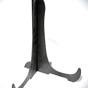May include: A black metal display stand with three legs. The stand is designed to hold a plate or other flat object.