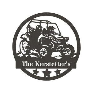 May include: Black and white silhouette of a side-by-side ATV with two riders in a circle with five stars and the text "The Kerstetter's" below.