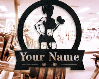 May include: Black metal wall art featuring a silhouette of a weightlifting figure inside a circular frame. The figure is holding dumbbells. The text "Your Name" is displayed on a banner below the figure. The background is a blurred gym setting.