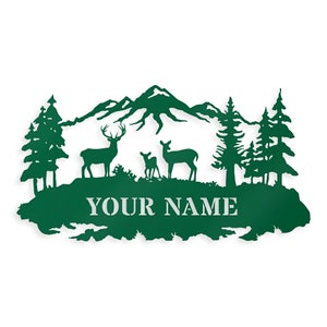 May include: Green metal silhouette of a mountain range with two deer and a fawn standing in front of a forest. The text "YOUR NAME" is below the deer.