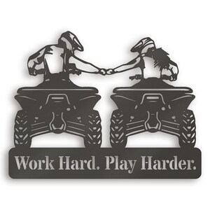 May include: Black metal silhouette of two people riding quad bikes, holding hands, with the text "Work Hard. Play Harder." below.