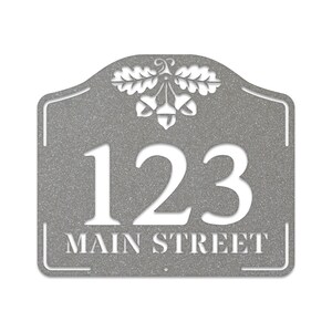 May include: A gray metal house number sign with an acorn and oak leaf design. The number 123 and the text "MAIN STREET" are cut out in white.