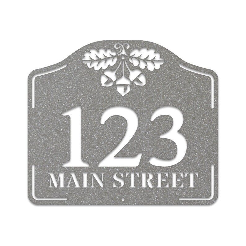 May include: A gray metal house number sign with an acorn and oak leaf design. The number 123 and the text "MAIN STREET" are cut out in white.