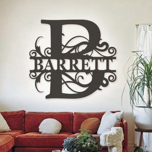 May include: A large, dark brown, wall-mounted metal sign featuring a decorative capital letter B with intricate scrollwork patterns. The name BARRETT is cut out in capital letters across the center of the letter, creating a personalized display.