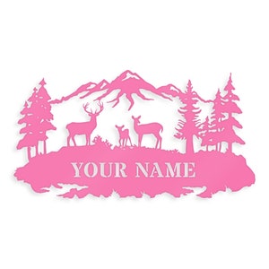May include: Pink metal silhouette of a mountain range with two deer and a fawn standing in front of a forest. The text "YOUR NAME" is written below the deer.