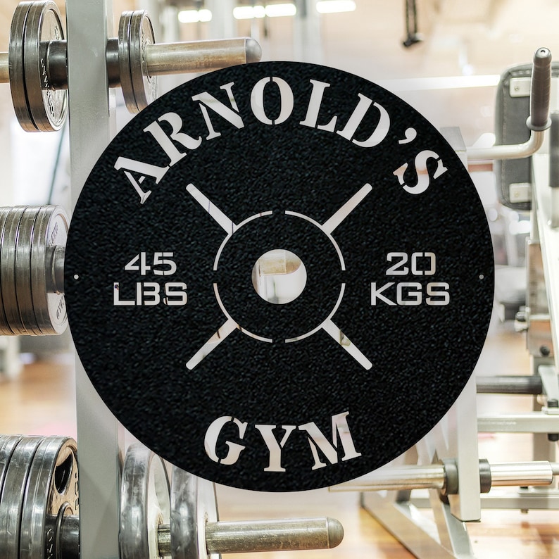 May include: Black metal weight plate with white lettering that reads "Arnold's Gym" and "45 LBS 20 KGS".