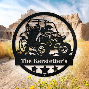 May include: Black metal silhouette of a four-wheeled off-road vehicle with two figures inside, set against a scenic backdrop. The text "The Kerstetter's" is displayed below the vehicle, along with three stars.