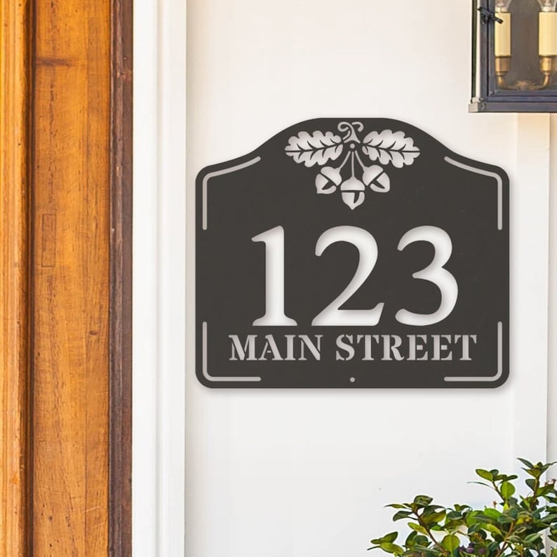 May include: Black metal house number sign with an acorn design and the address 123 Main Street.