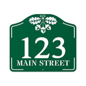May include: Green metal house number sign with white lettering. The sign features an acorn and oak leaf design and the address 123 Main Street.