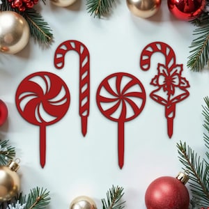 May include: Four red Christmas-themed cake toppers. Two are candy canes, one is a candy swirl, and one is a candy cane with a bell and bow.