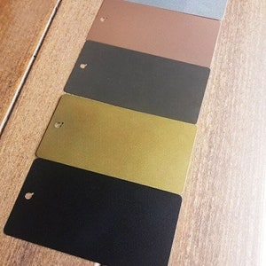 Pu&ograve; includere: Cinque campioni di colore di vernice su una superficie di legno. I colori sono blu chiaro, marrone, grigio scuro, oro e nero.