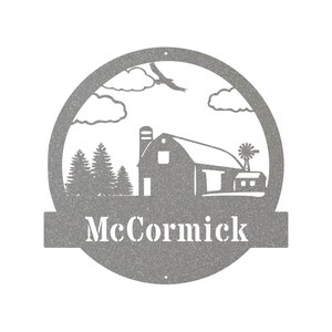 May include: A gray metal sign with a farmhouse silhouette, clouds, and trees. The sign has a banner at the bottom with the name "McCormick" in white lettering.