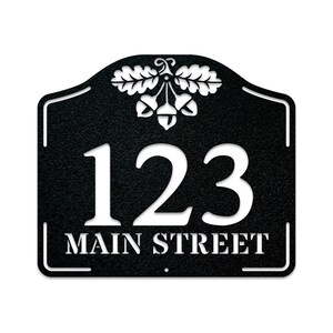 May include: Black metal house number sign with an acorn and oak leaf design. The sign reads "123 MAIN STREET".