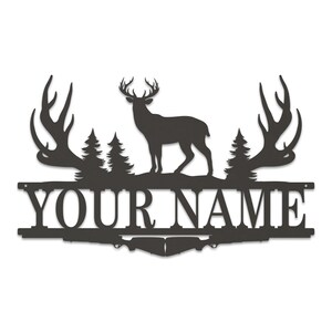 May include: Black metal silhouette of a deer with large antlers, standing in front of two pine trees. The deer is standing on a metal bar with the text "YOUR NAME" in black.