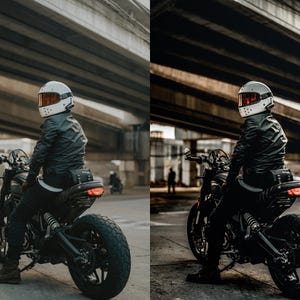 May include: A rider wearing a white full-face helmet with an orange visor and a black leather jacket sits on a black motorcycle. The motorcycle features a textured seat, a rear tail light, and thick tread tires, positioned under a concrete bridge.