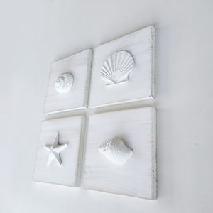 May include: Set of four white wooden wall decor pieces with raised seashell and starfish designs. Each piece features a different seashell or starfish.