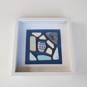Könnte beinhalten: Ein gerahmtes Kunstwerk mit einer Sammlung von blauen und weißen Keramikfliesen, die in einem geometrischen Muster auf einem dunkelblauen Hintergrund angeordnet sind.