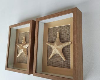 Décoration murale rustique de plage avec des étoiles de mer dorées, deux tableaux encadrés et une œuvre d'art côtière moderne.