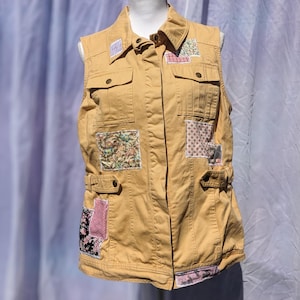 May include: A yellow utility vest with multiple pockets and patches of floral fabric. The vest has a button-up front and a belt.