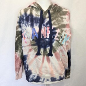 Peut inclure: Un sweat à capuche tie-dye dans les tons de bleu, rose, vert et blanc. Le mot "FRANKLIN" est appliqué sur la poitrine dans divers tissus à motifs. Le sweat à capuche a un cordon de serrage et une poche avant.