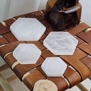Può includere: Quattro piastre di ricarica in selenite esagonali bianche di diverse dimensioni su una superficie in pelle marrone.
