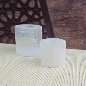 Pu&ograve; includere: Due portacandele in selenite bianca di diverse dimensioni. Il portacandele pi&ugrave; grande &egrave; sullo sfondo e quello pi&ugrave; piccolo &egrave; in primo piano. Entrambi i portacandele sono realizzati in cristallo di selenite e hanno una texture naturale e ruvida.