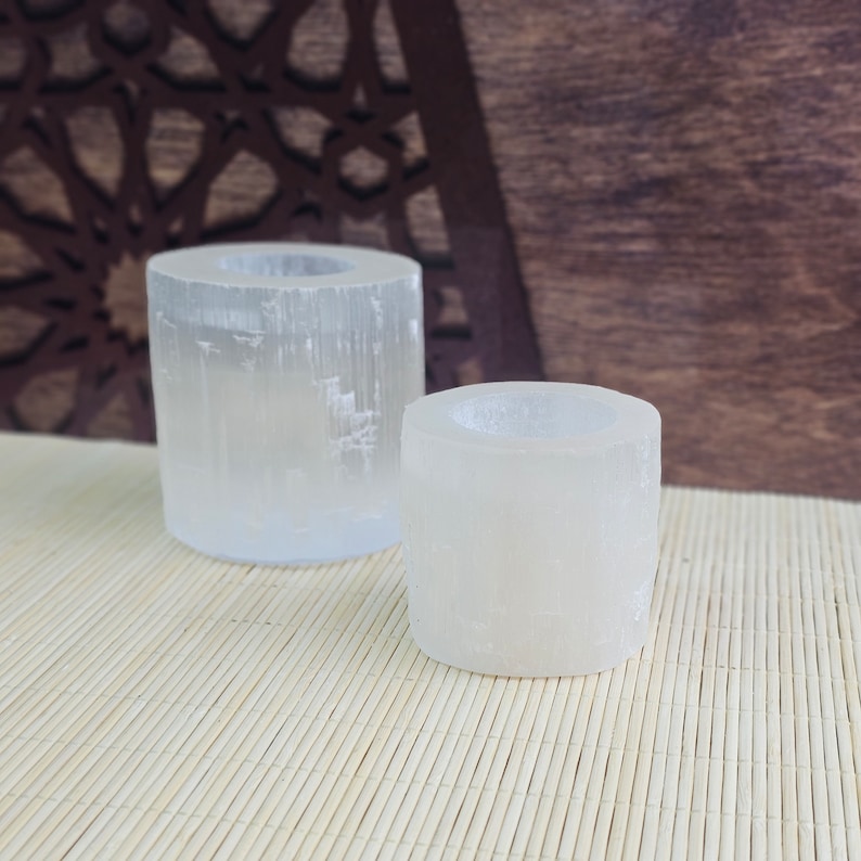 Pu&ograve; includere: Due portacandele in selenite bianca di diverse dimensioni. Il portacandele pi&ugrave; grande &egrave; sullo sfondo e quello pi&ugrave; piccolo &egrave; in primo piano. Entrambi i portacandele sono realizzati in cristallo di selenite e hanno una texture naturale e ruvida.