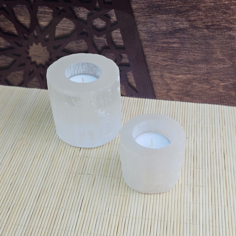 Pu&ograve; includere: Due portacandele in selenite bianca con forma rotonda e cilindrica. I portacandele sono su un tappetino di bamb&ugrave; marrone chiaro.