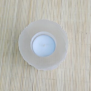 Pu&ograve; includere: Un portacandele bianco in cristallo di selenite naturale di forma rotonda e superficie liscia e lucida. Il portacandele ha un'apertura circolare al centro per contenere una candela tea light.