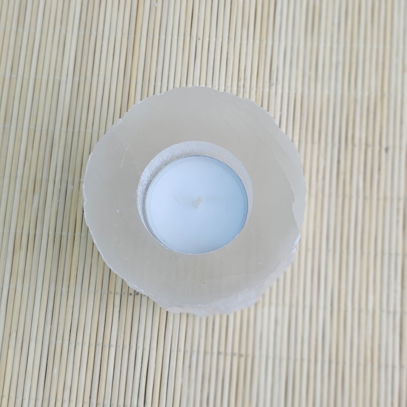 Pu&ograve; includere: Un portacandele bianco in cristallo di selenite naturale di forma rotonda e superficie liscia e lucida. Il portacandele ha un'apertura circolare al centro per contenere una candela tea light.