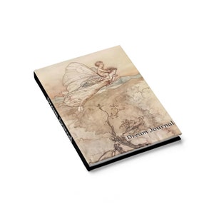 May include: A dream journal with a black cover and a vintage illustration of a fairy carrying a child. The text "Dream Journal" is printed on the cover.