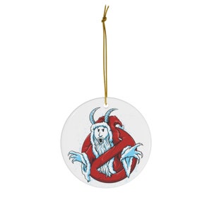 Op de afbeelding: Een witte kerstversiering van keramiek met een blauwe en witte geest die een rode kerstmanmuts en een rood en wit kerstmanpak draagt. De geest wordt omringd door een rode cirkel met een diagonale lijn erdoorheen, vergelijkbaar met het "Ghostbusters"-logo.