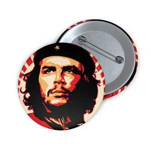 May include: A red, white, and black button featuring a portrait of Che Guevara. The button has a silver back with a safety pin.