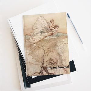 May include: A vintage-style journal with a watercolor illustration of a fairy flying with a child on her back. The journal cover has the text "Dream Journal" printed on it.