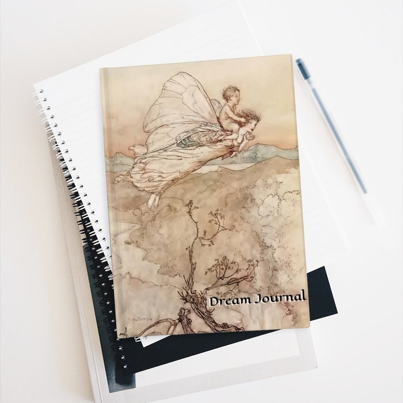May include: A vintage-style journal with a watercolor illustration of a fairy flying with a child on her back. The journal cover has the text "Dream Journal" printed on it.