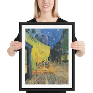Puede incluir: Una impresión enmarcada de una pintura de Vincent van Gogh que representa un café por la noche con un cielo estrellado. El café está iluminado con luz amarilla y hay gente sentada en mesas afuera. La pintura está en un marco negro.