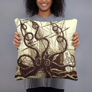 May include: A cream-colored throw pillow with a vintage illustration of a giant octopus attacking a sailing ship. The octopus is brown and the ship is detailed with rigging and sails.