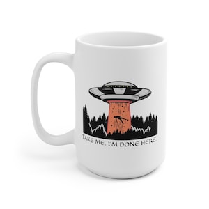 May include: White ceramic mug with a black and white illustration of a UFO hovering over a forest with the text "Take me. I'm done here."