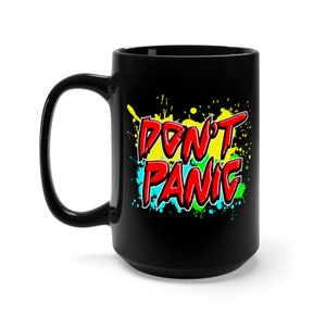 May include: Black ceramic mug with a white background and colorful paint splatters. The text "DON'T PANIC" is written in red letters.