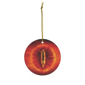 May include: A round ceramic bauble featuring a red and orange eye design. The eye is a deep yellow colour with a black pupil.