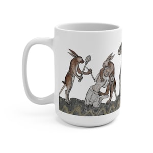 May include: A white ceramic mug with a medieval illustration of three rabbits attacking a person. The rabbits are brown and white, and the person is wearing a white robe. The background is a green and brown landscape.