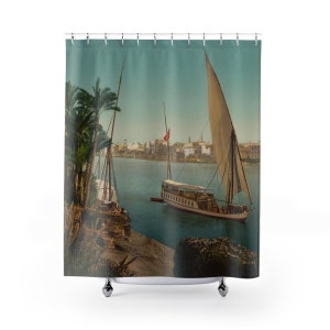 May include: A vintage photograph of two sailboats on a river in front of a city skyline. The boats are white with brown sails and red flags. The river is blue and the sky is a light blue. The city skyline is in the background and is made up of buildings with red roofs.