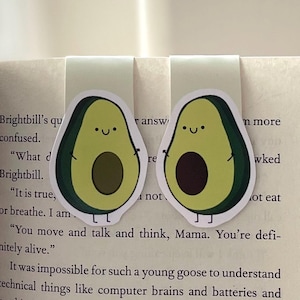 May include: Two avocado-shaped bookmarks with smiling faces. The bookmarks are green with brown pits and are holding hands. The text "You move and talk and think, Mama. You're definitely alive." is visible in the background.